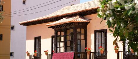 Un edificio con techo de tejas, ventanas grandes y macetas con plantas en el balcón.