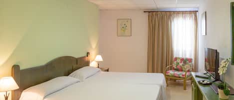 A hotel room with two beds, a desk with a TV, a chair, and a window with curtains.