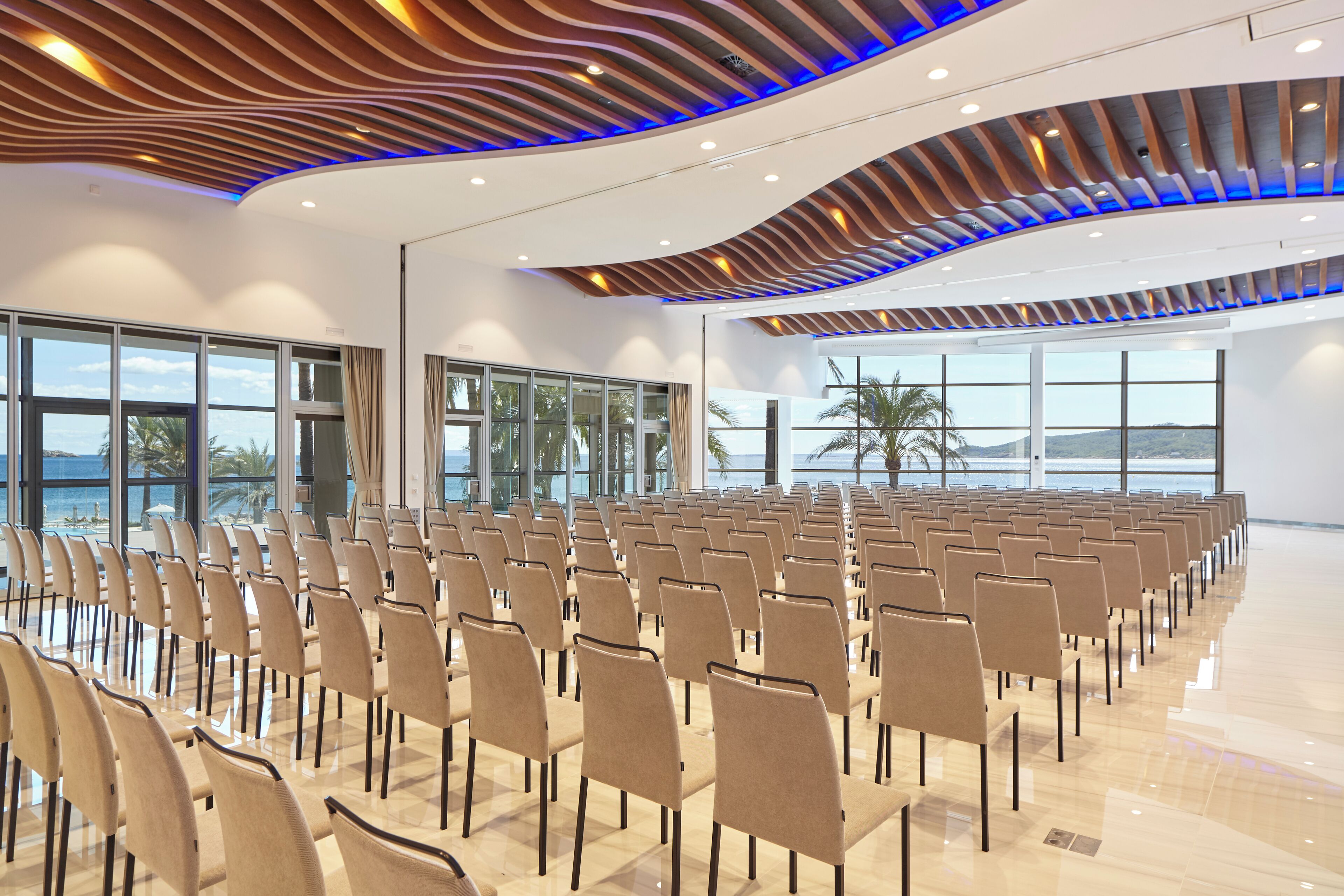 Un salón de conferencias con filas de sillas, ventanas amplias y un diseño moderno del techo.