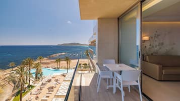 Un balcón con vistas al mar, una piscina y un área de descanso con sillas y mesas.