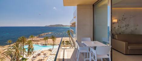A balcony with a view of the sea, a pool, and a lounge area with chairs and tables.
