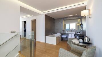 Una habitación de hotel moderna con una escalera de cristal, una zona de estar con una pequeña mesa, una bañera y una kitchenette.