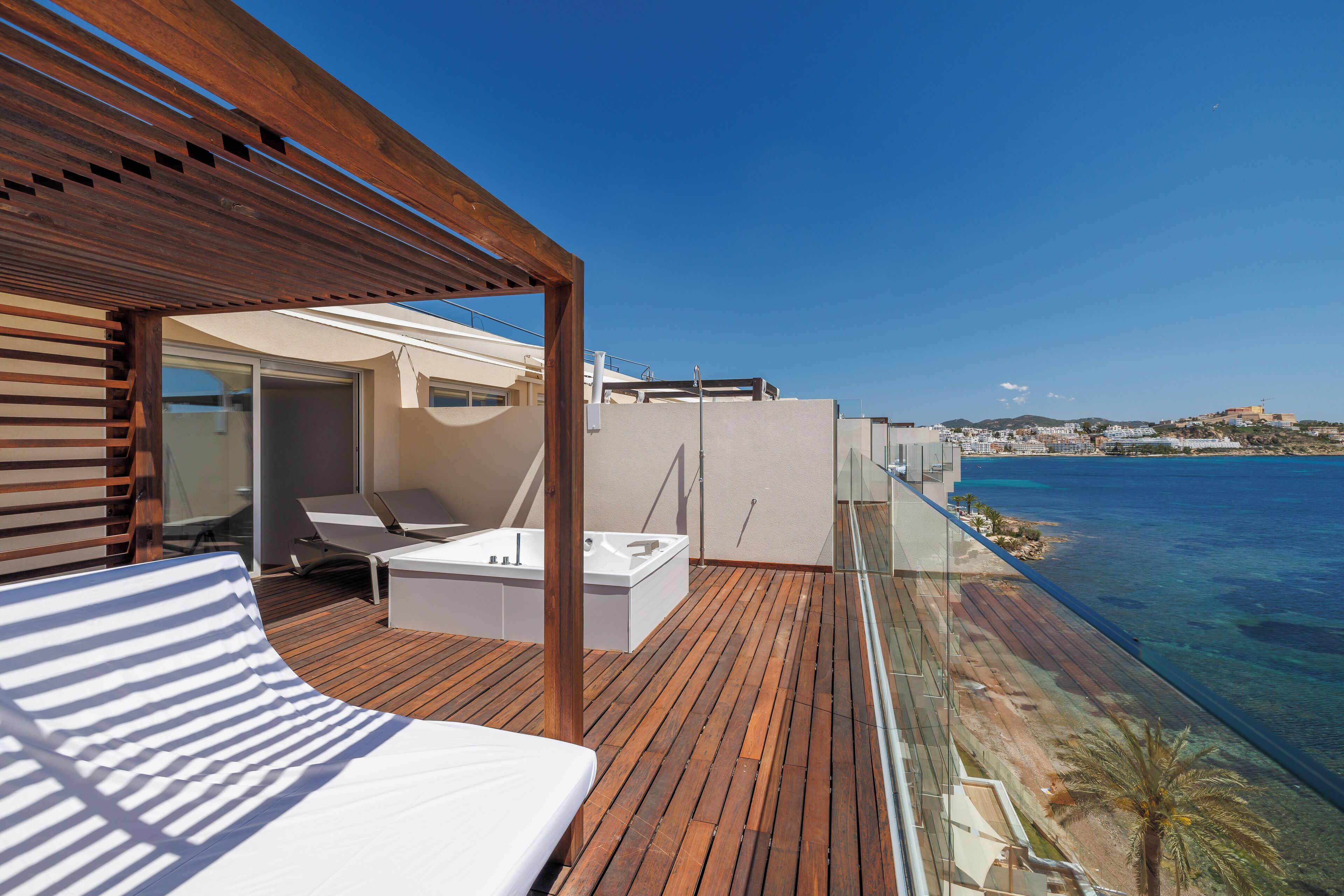 A wooden deck with a bed, a bathtub, and a lounge chair.