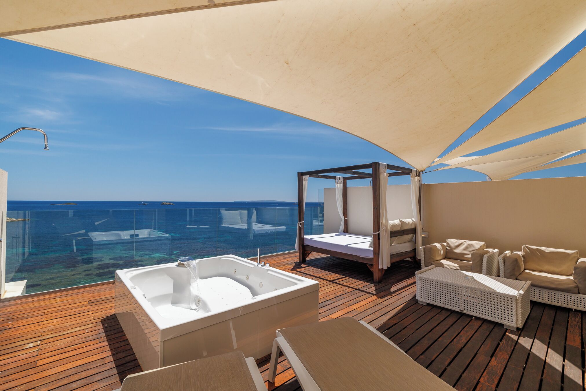 Une terrasse ensoleillée dotée d’un jacuzzi, de chaises longues et d’un auvent offrant une vue sur l’océan.