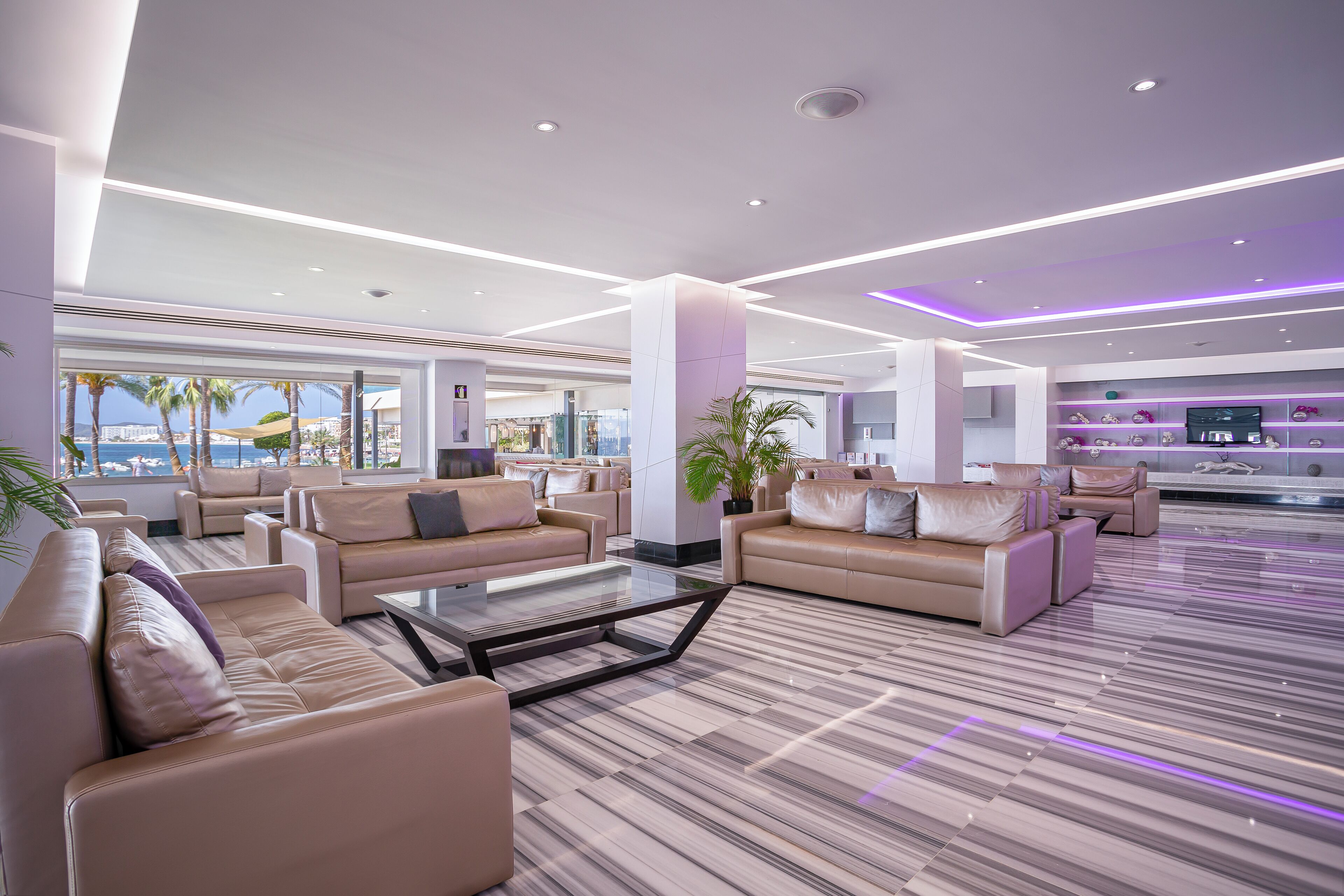 A spacious lobby with leather sofas, a glass coffee table, and a view of the beach.