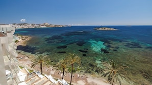 Un hotel frente al mar, con vista despejada, palmeras y una isla rocosa en la distancia.