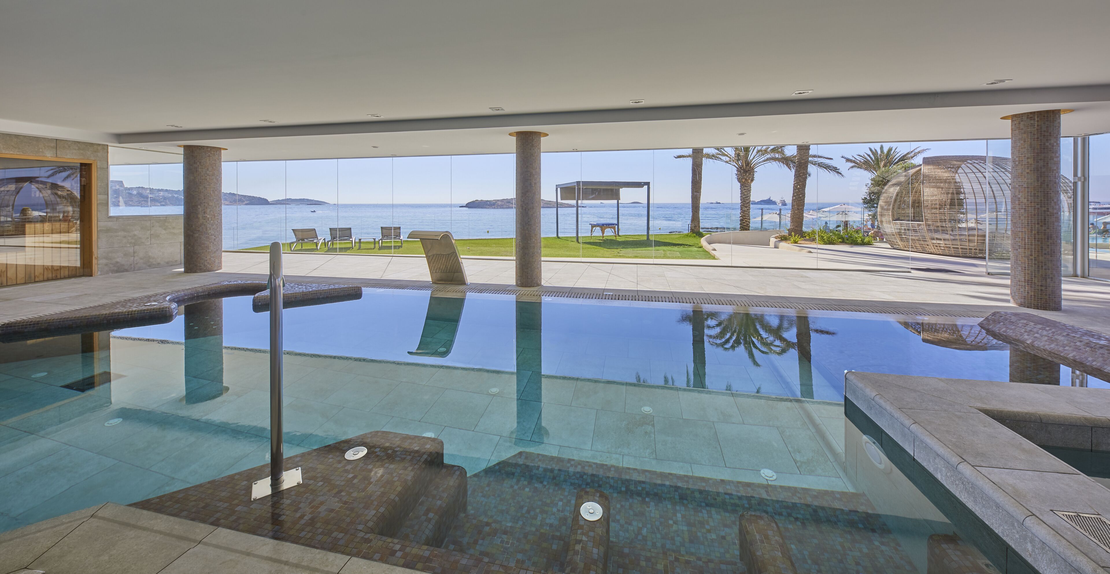 An infinity pool with clear views of the sea and palm trees.