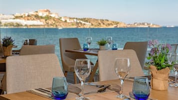 Mesa lista para comer con vista al mar y una colina distante.