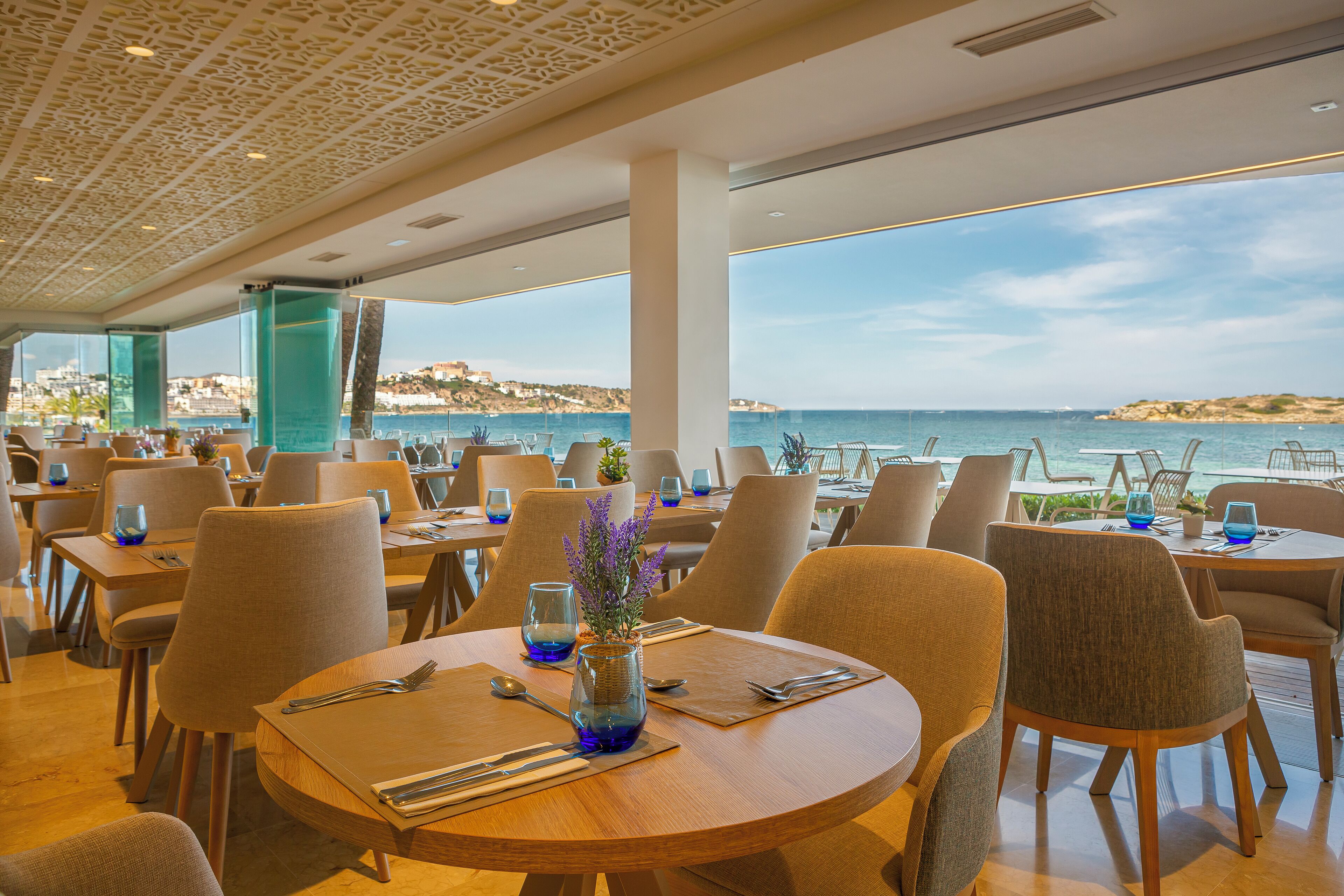 Un restaurante con mesas redondas, sillas y vista al mar.