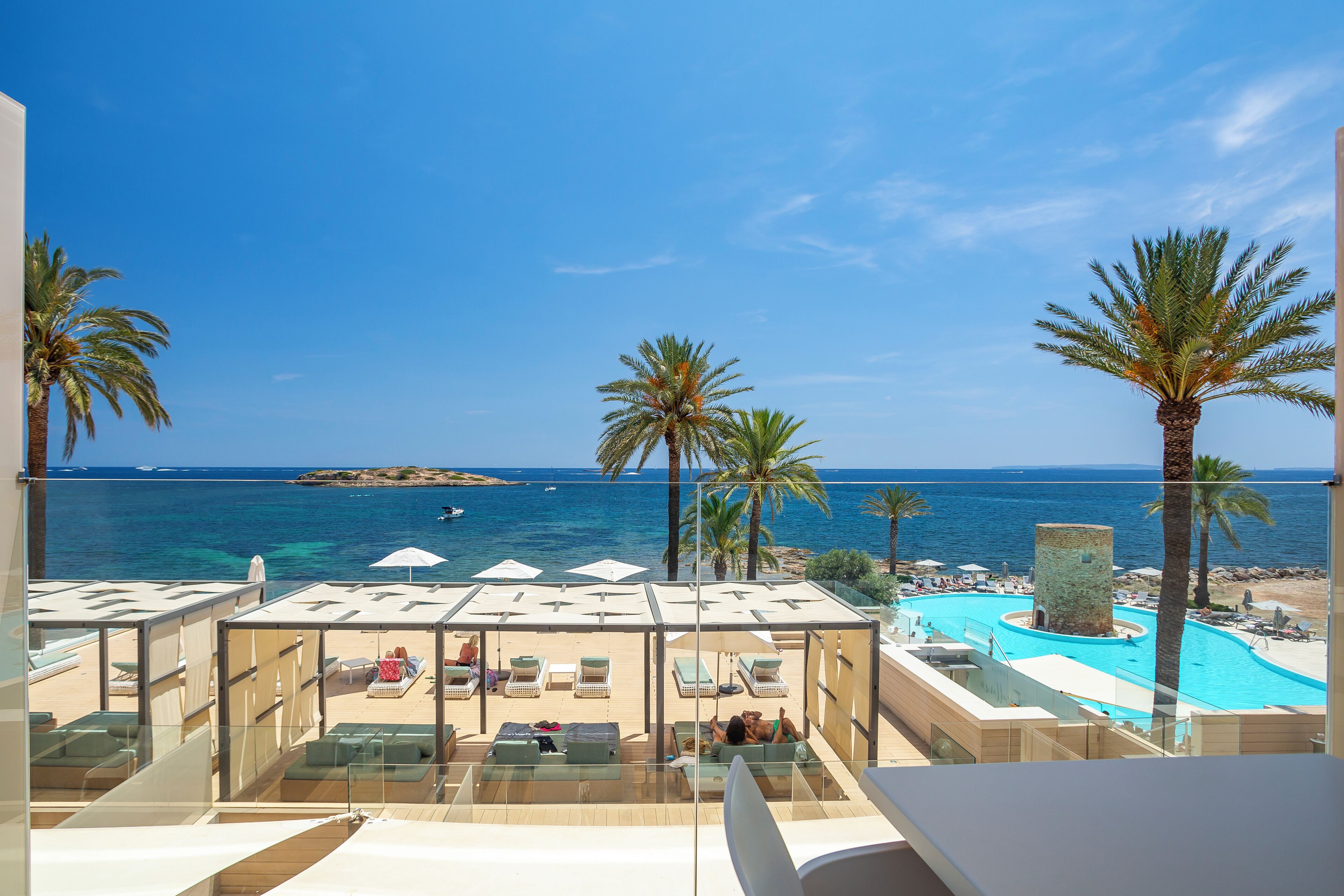 A poolside area with lounge chairs and umbrellas, overlooking a beach and the sea.