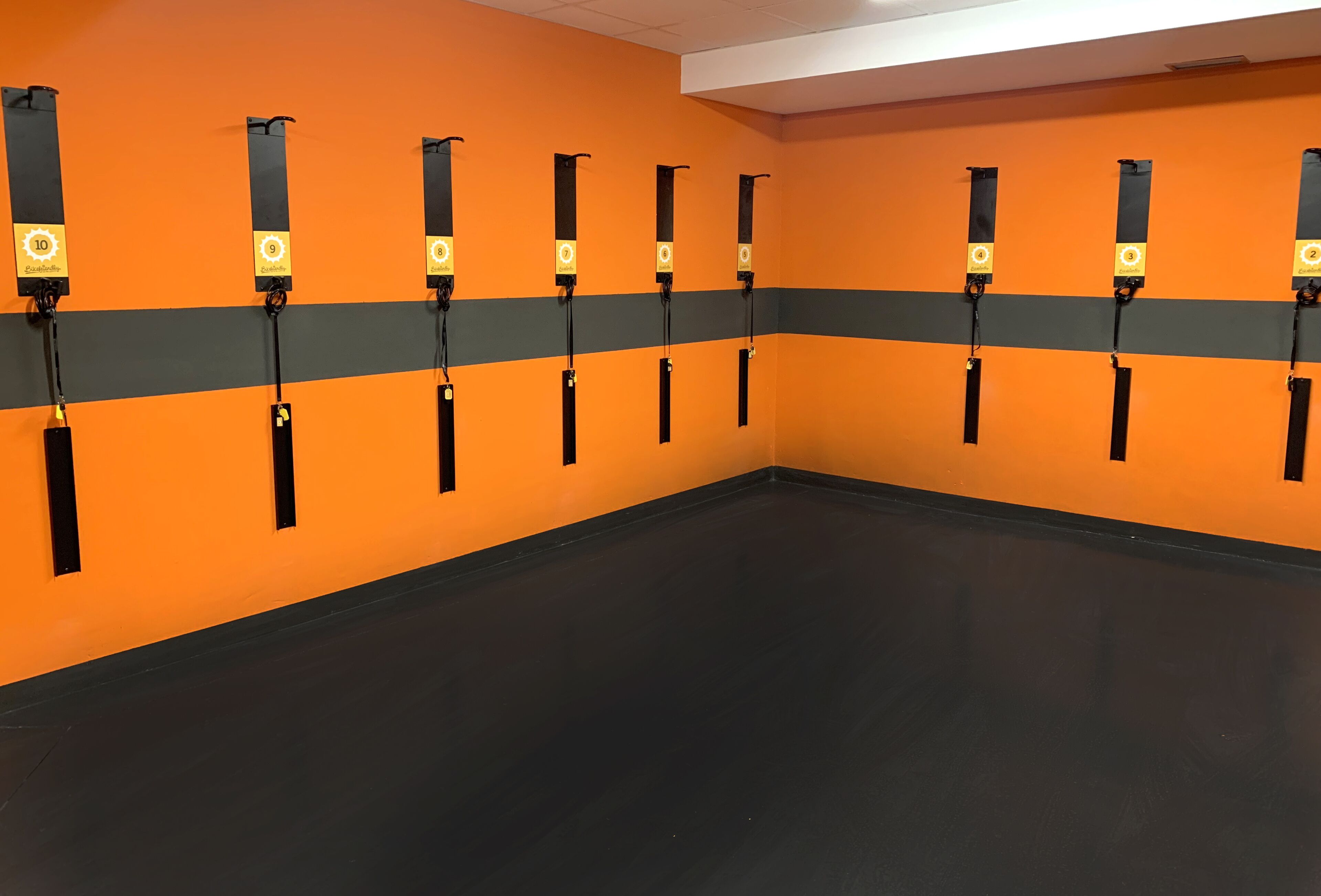 Ein Raum mit orangefarbenen Wänden und schwarzem Boden, ausgestattet mit mehreren Trainingsgeräten.