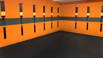 Ein Raum mit orangefarbenen Wänden und schwarzem Boden, ausgestattet mit mehreren Trainingsgeräten.