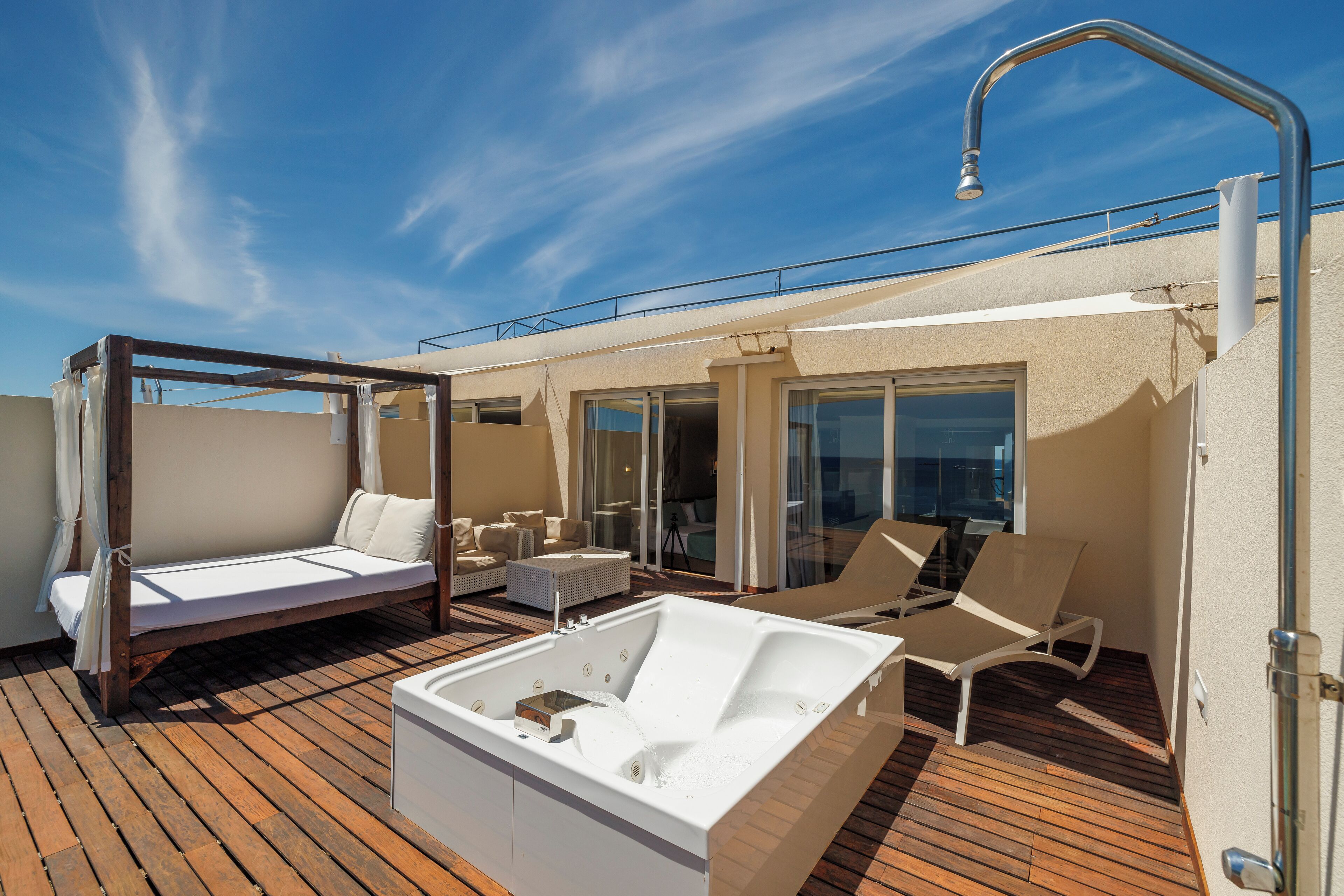 A sunlit outdoor deck with a hot tub, lounge chairs, and a canopy bed.
