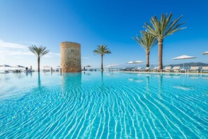 A pool with clear blue water, surrounded by palm trees and lounge chairs under umbrellas. - Hotel Torre Del Mar (Ibiza Town)