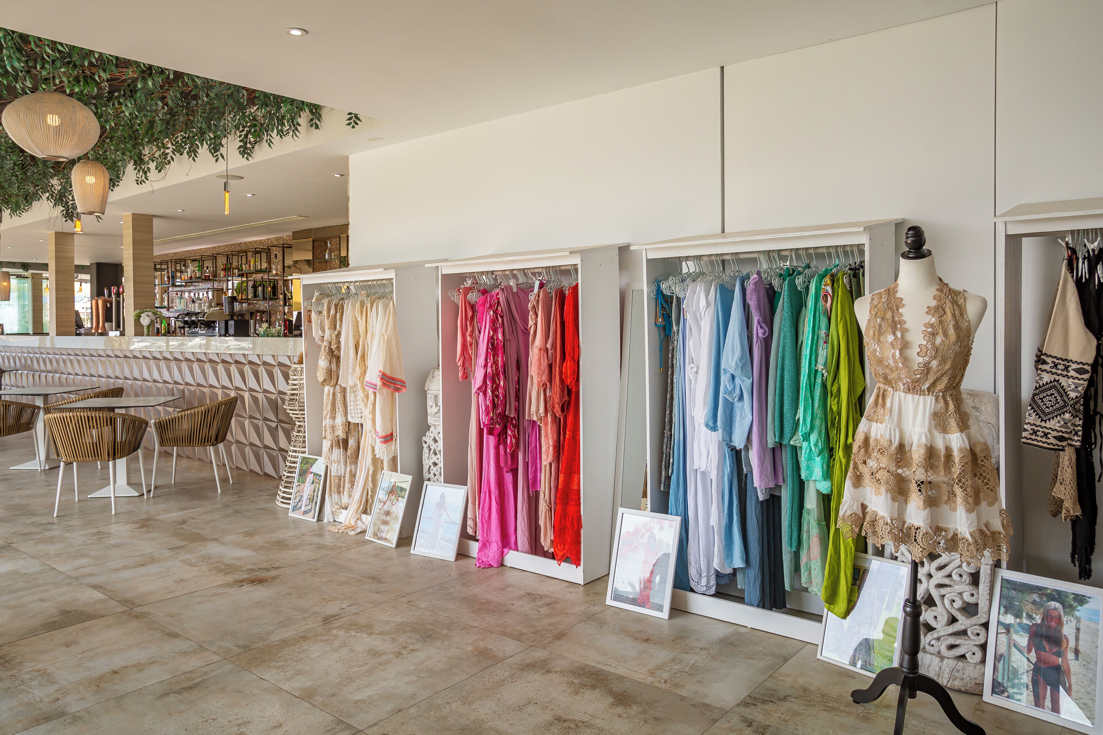 A boutique hotel interior with a seating area, a bar, and a clothing display with mannequins and racks of dresses.