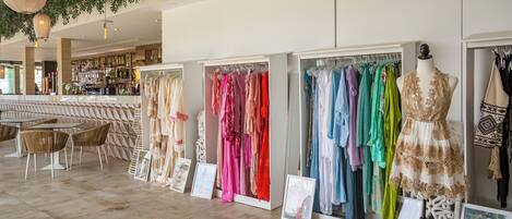 A boutique hotel interior with a seating area, a bar, and a clothing display with mannequins and racks of dresses.
