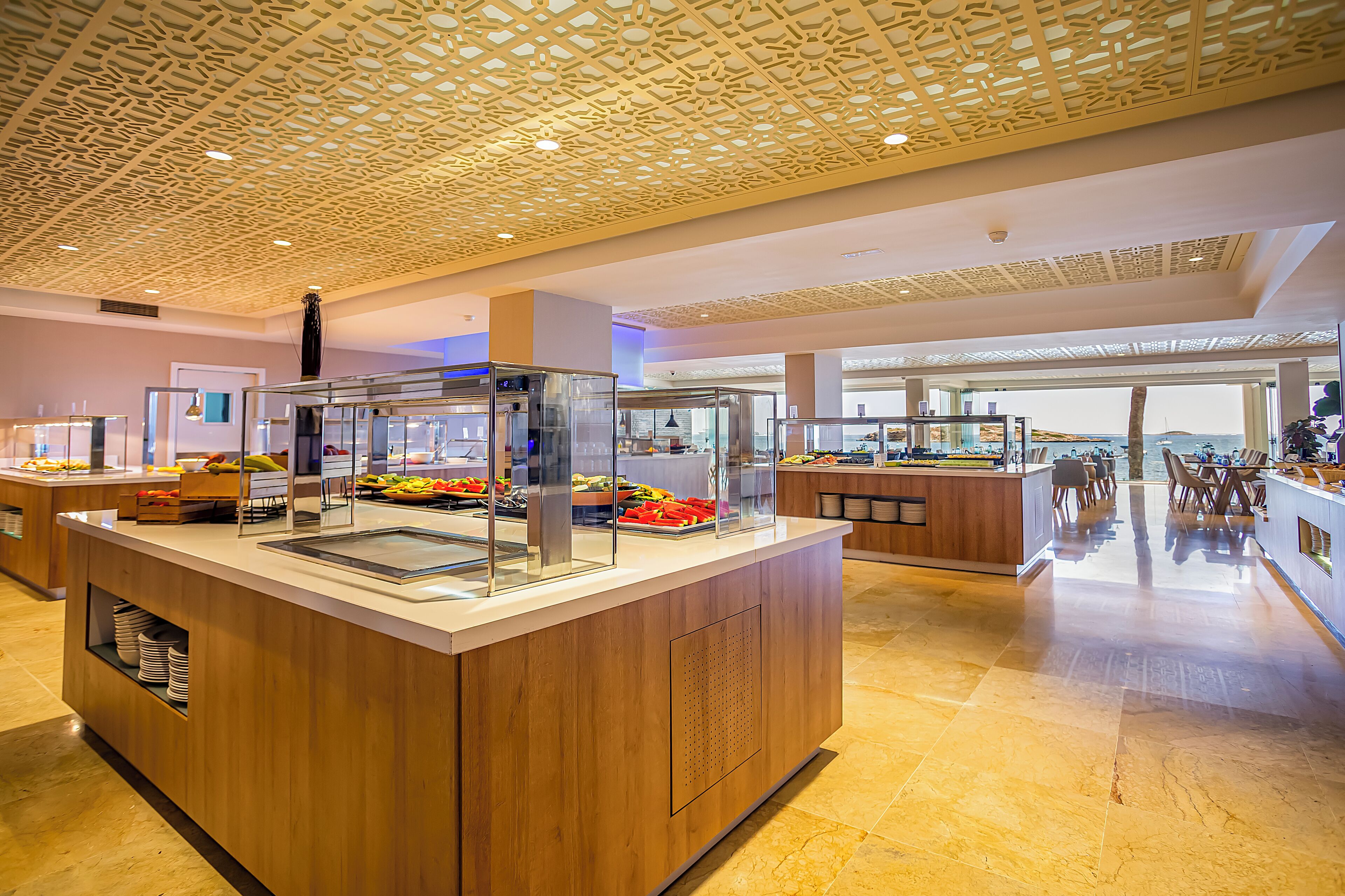 Un espace moderne dédié au petit-déjeuner, avec des comptoirs en bois, des vitrines et une vue sur la mer.