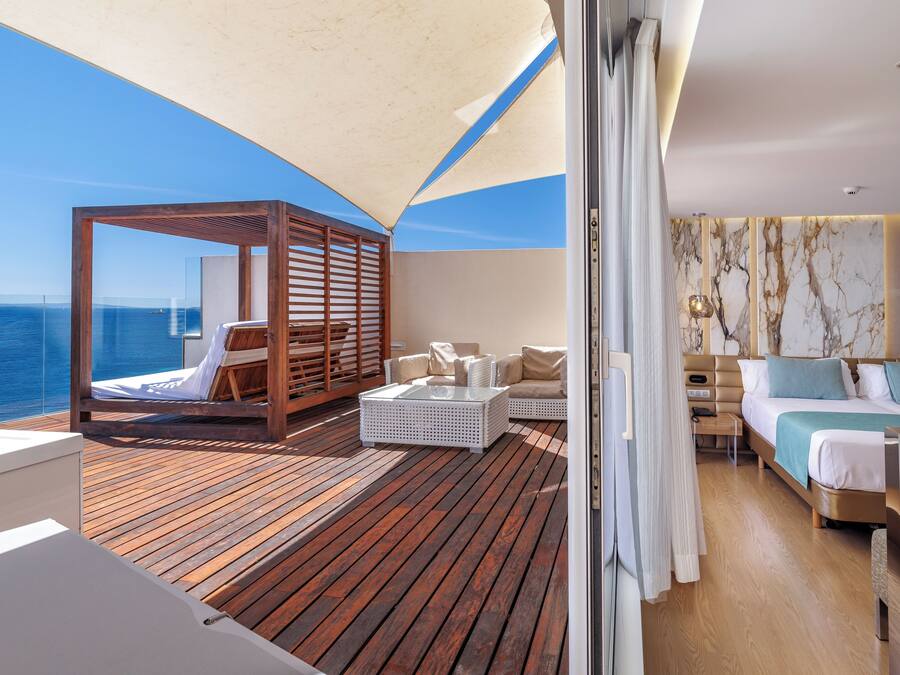 Un balcón con suelo de madera, una zona de estar con toldo de madera y una cama frente a una pared de mármol.