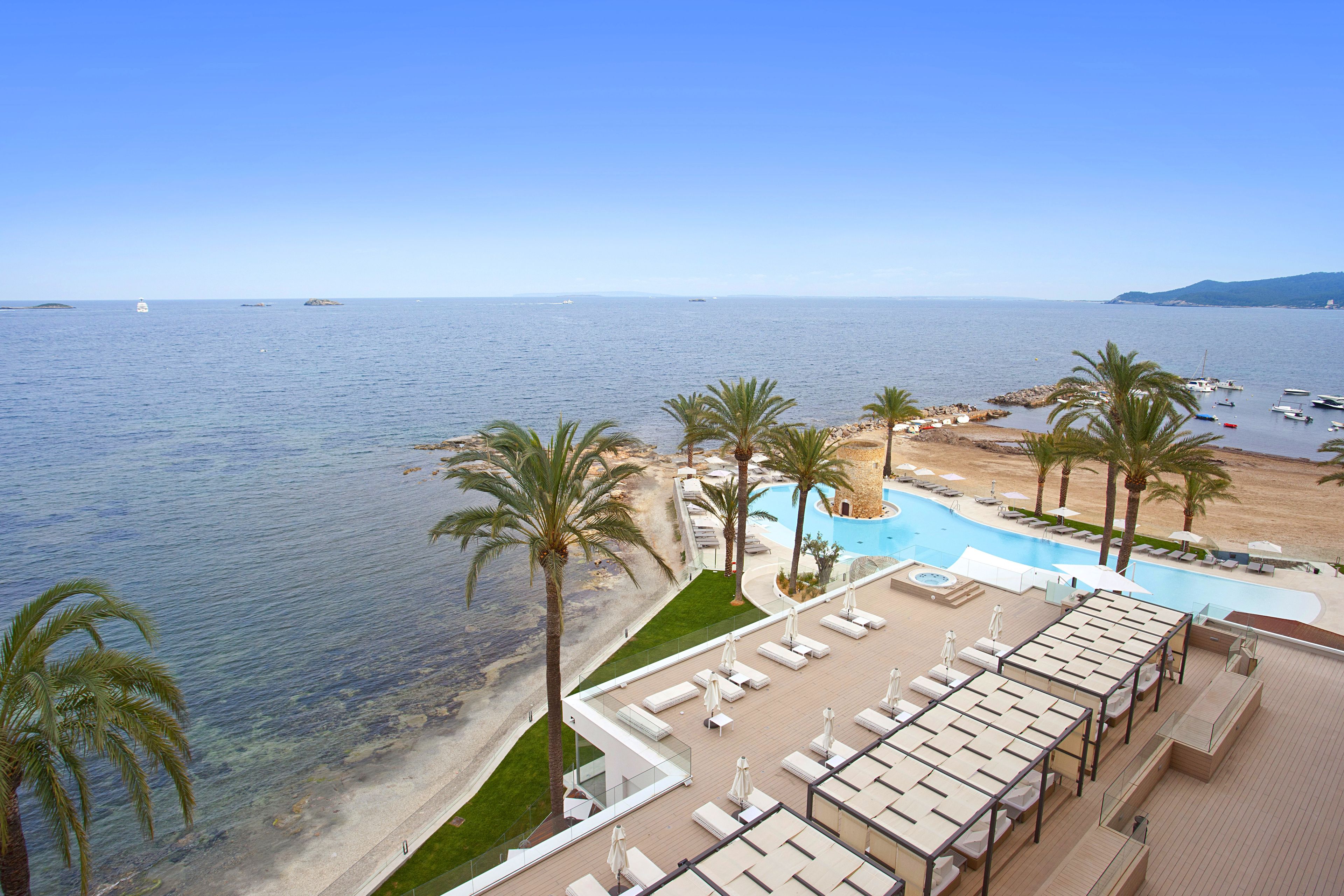 Un resort con piscina, sillones de descanso y vista al mar.