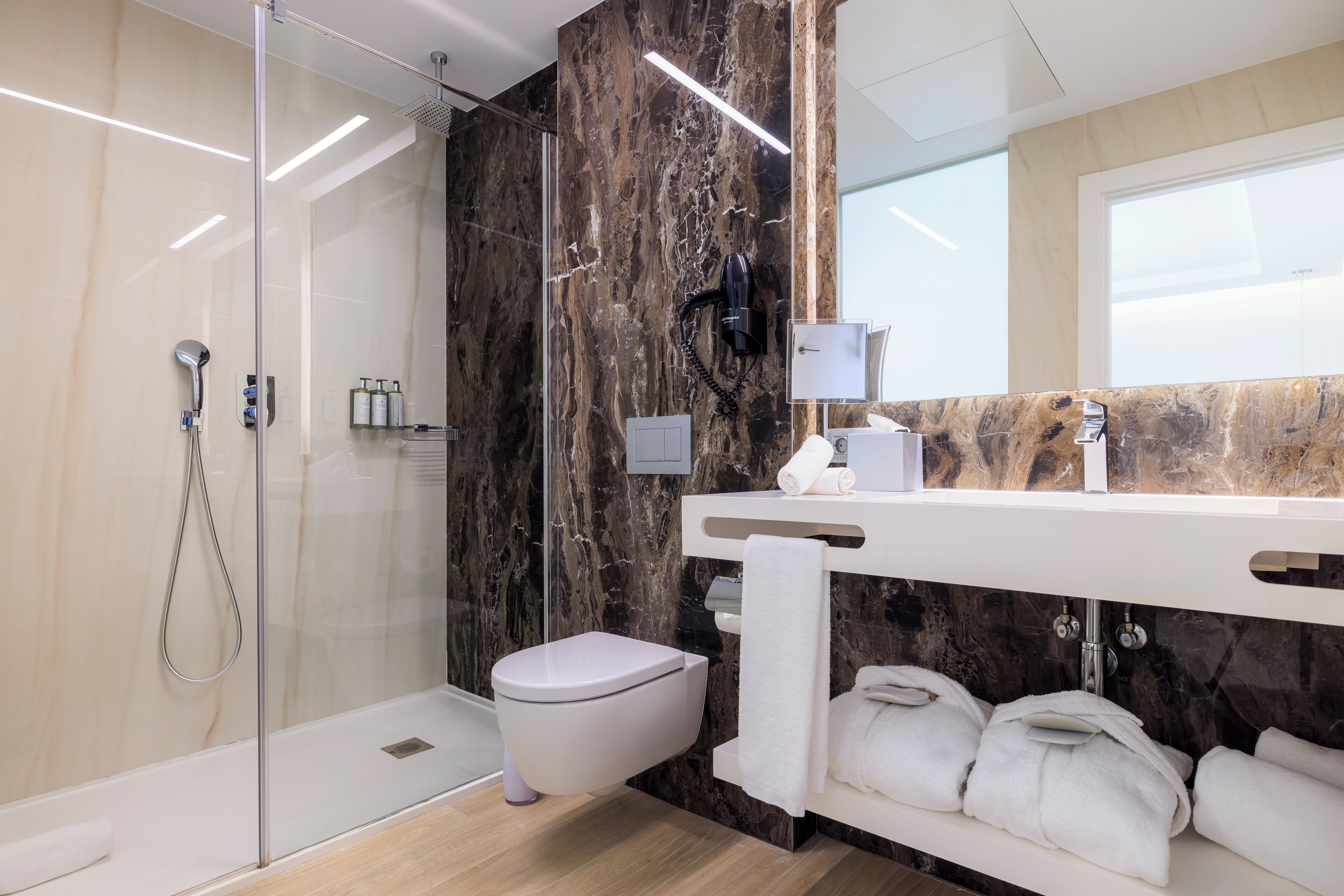 Un baño moderno con ducha de vidrio, inodoro blanco y pared de mármol.