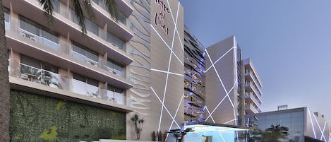Un hotel moderno con una fachada geométrica única y un área exterior bien cuidada con palmeras y un jardín paisajístico.
