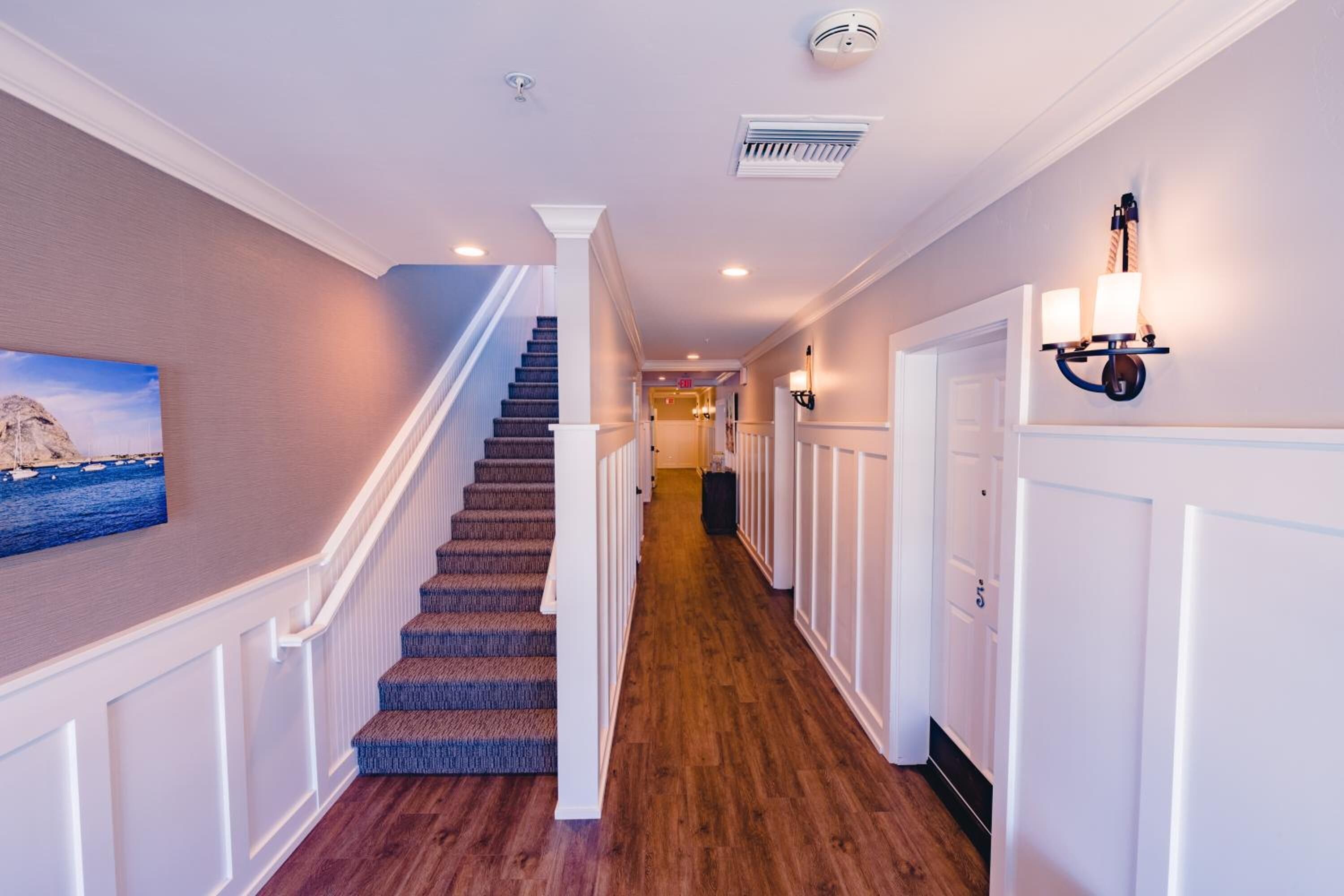 A hallway with a carpeted staircase, white walls, and a painting of a ship on the left.