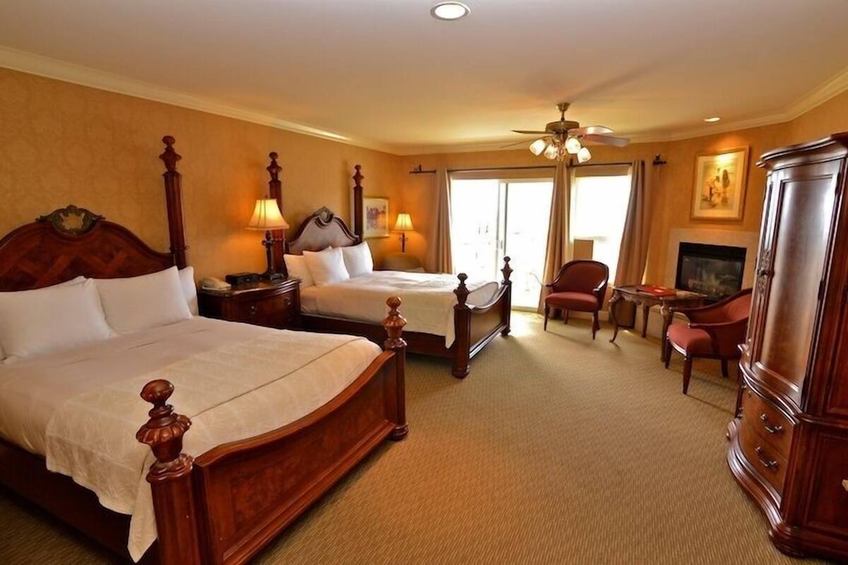 A hotel room with two wooden beds, a television, a fireplace, and a ceiling fan.