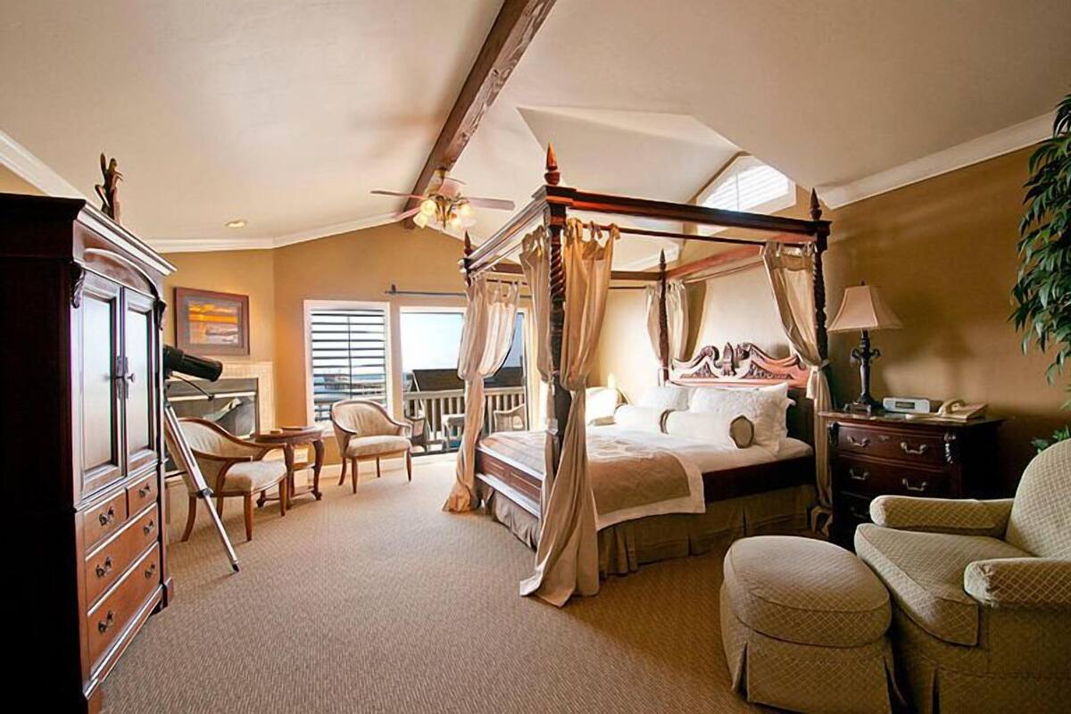 A four-poster canopy bed with a ceiling fan, a desk with a chair, and a large potted plant.