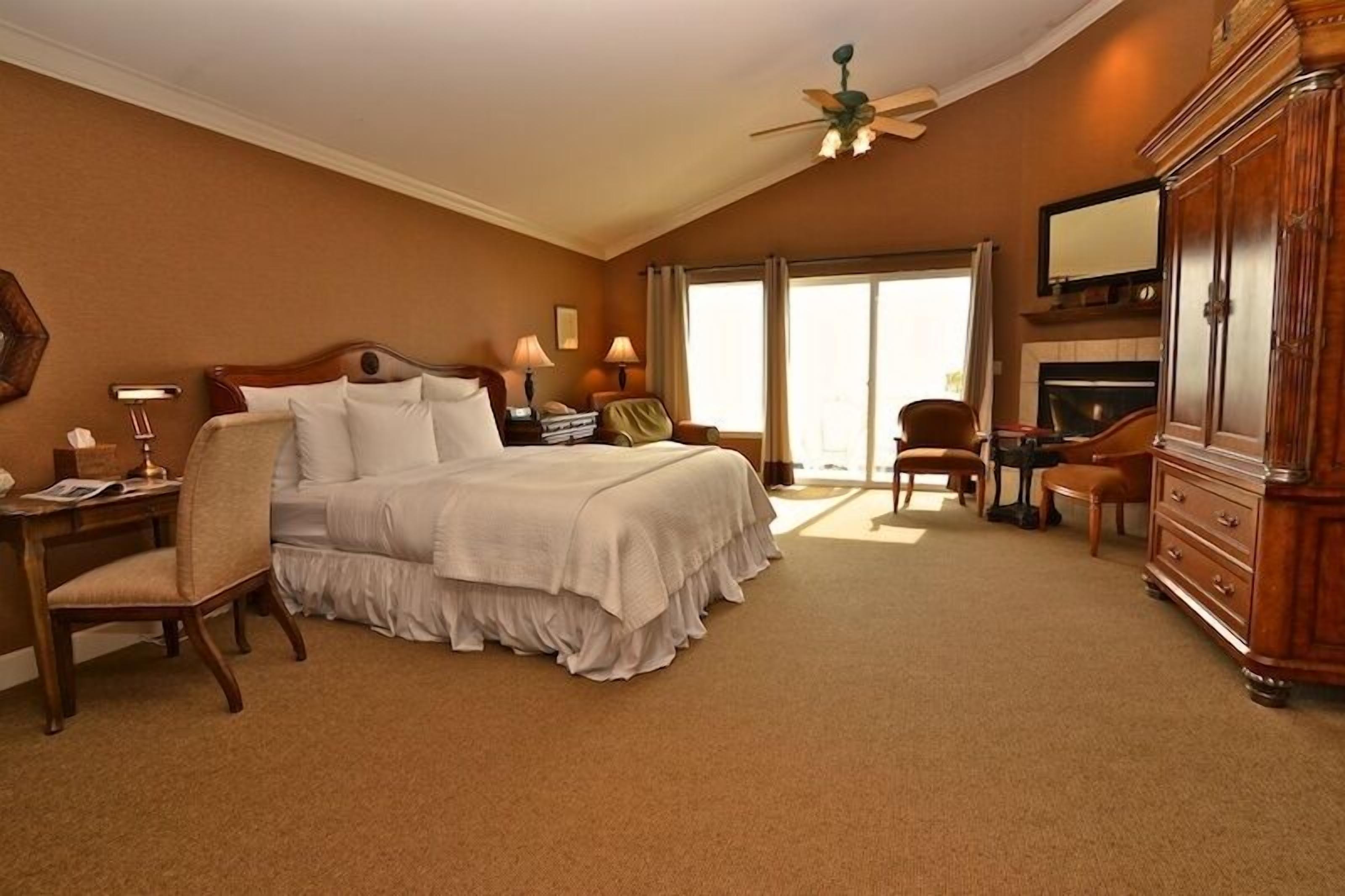 Une chambre d’hôtel avec un grand lit, un bureau avec une chaise, une coiffeuse avec un miroir et une cheminée.
