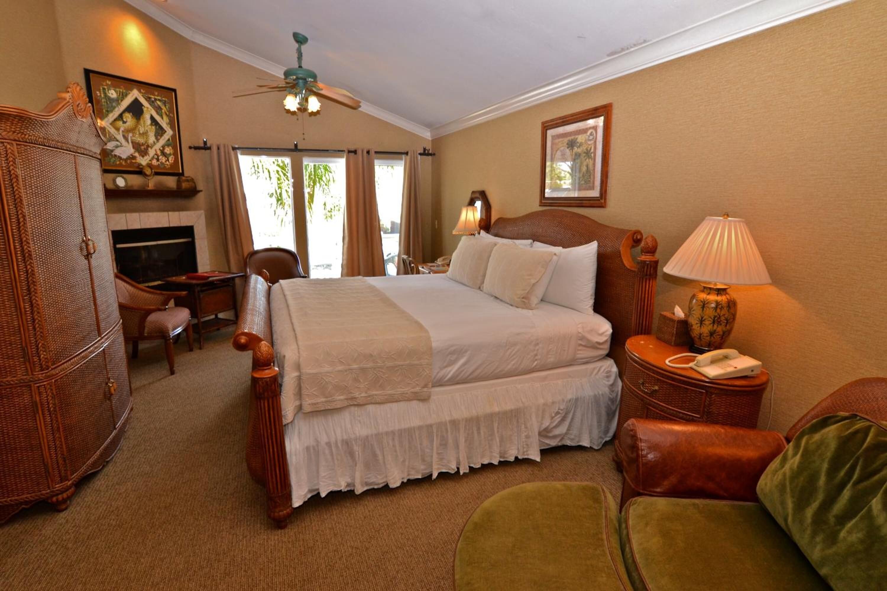 A hotel room with a large bed, a desk, a chair, a lamp, a telephone, and a fireplace.