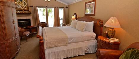 A hotel room with a large bed, a desk, a chair, a lamp, a telephone, and a fireplace.