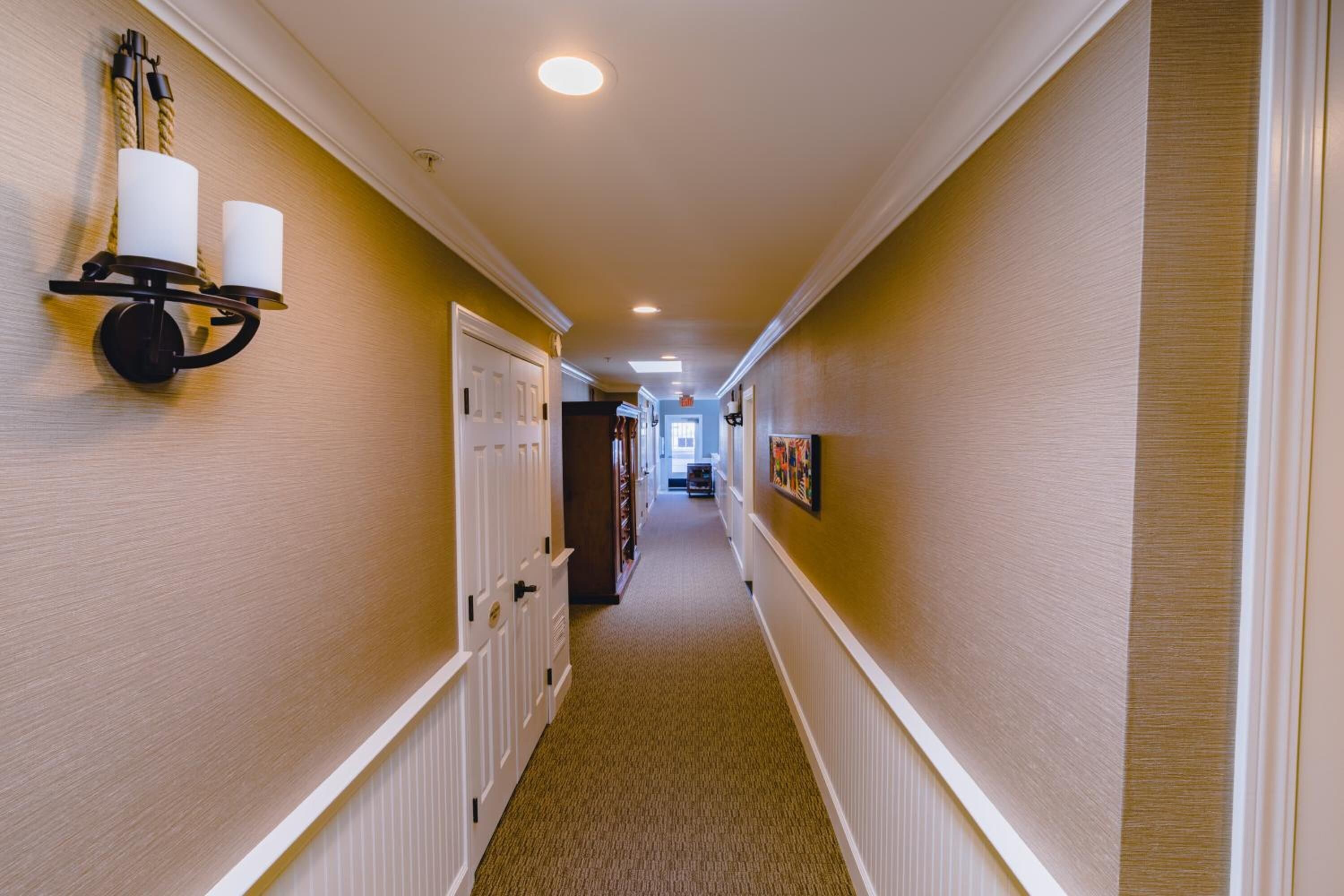 A hallway with a carpeted floor, white doors, and a wall-mounted light fixture with two candles.