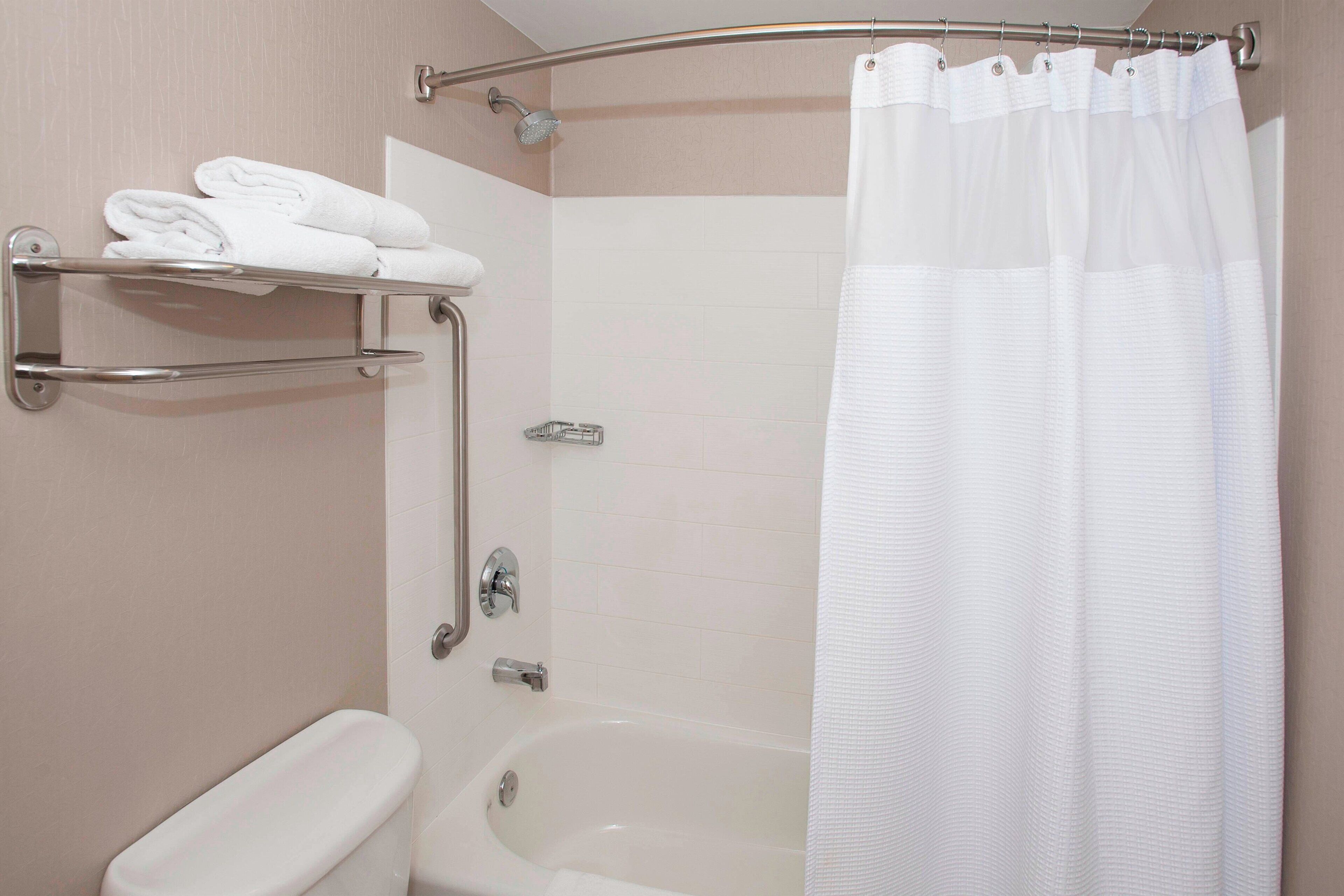 A bathroom with a bathtub, a toilet, a towel rack with folded towels, and a shower curtain.