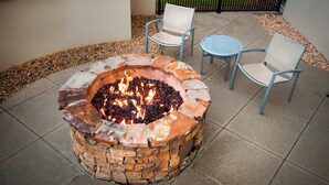 A stone fire pit with a fire burning, surrounded by two chairs and a small round table on a patio. - SpringHill Suites by Marriott Birmingham Colonnade (Birmingham)