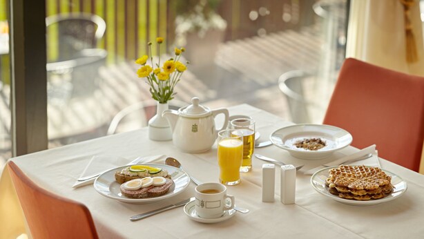 A breakfast table with plates of food, a teapot, glasses of orange juice, and a vase of yellow flowers. - Hotel Edda Akureyri (Akureyri)