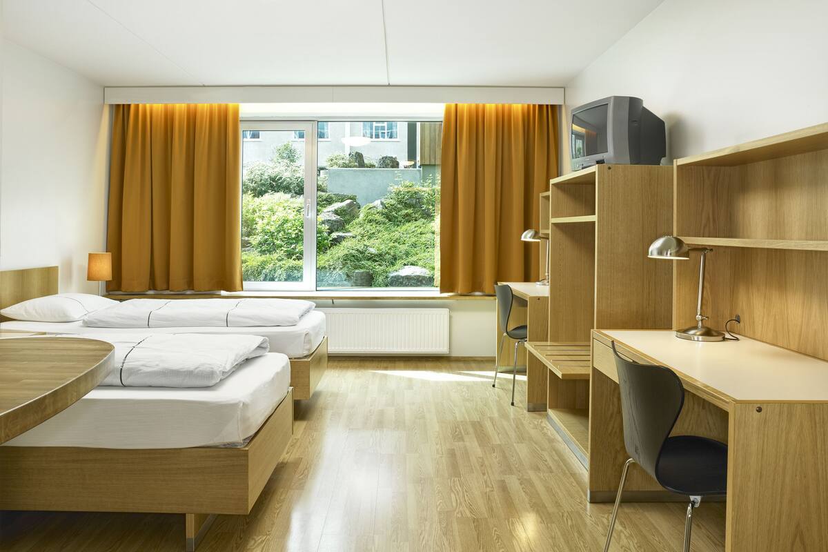 A hotel room with two beds, a desk, a chair, a TV, and a window with curtains.