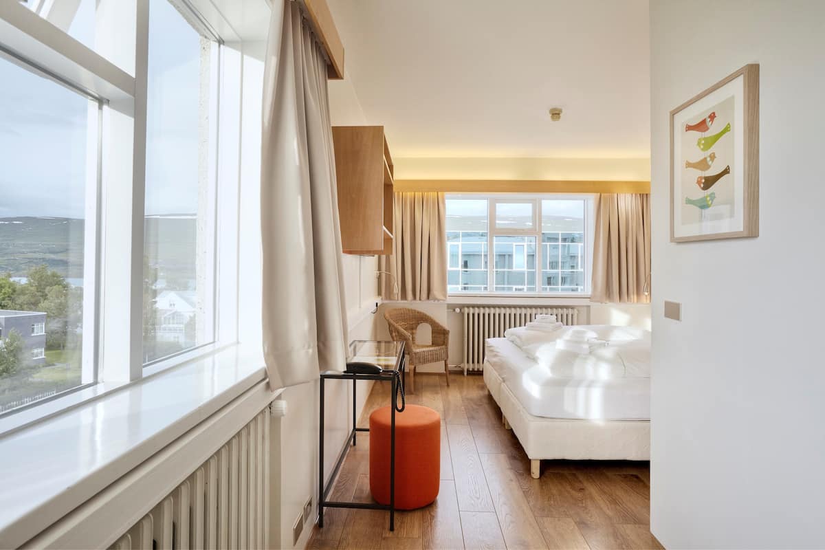 A bedroom with a large window, a bed, a chair, and a small table.