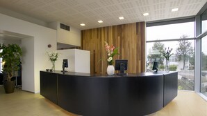 A modern reception desk with a curved design, a wooden accent wall, and large windows offering a view of the outdoors. - Hotel Edda Akureyri (Akureyri)