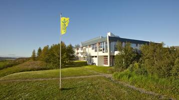 Un edificio moderno con techo plano y ventanas amplias, rodeado de follaje y un cielo despejado.