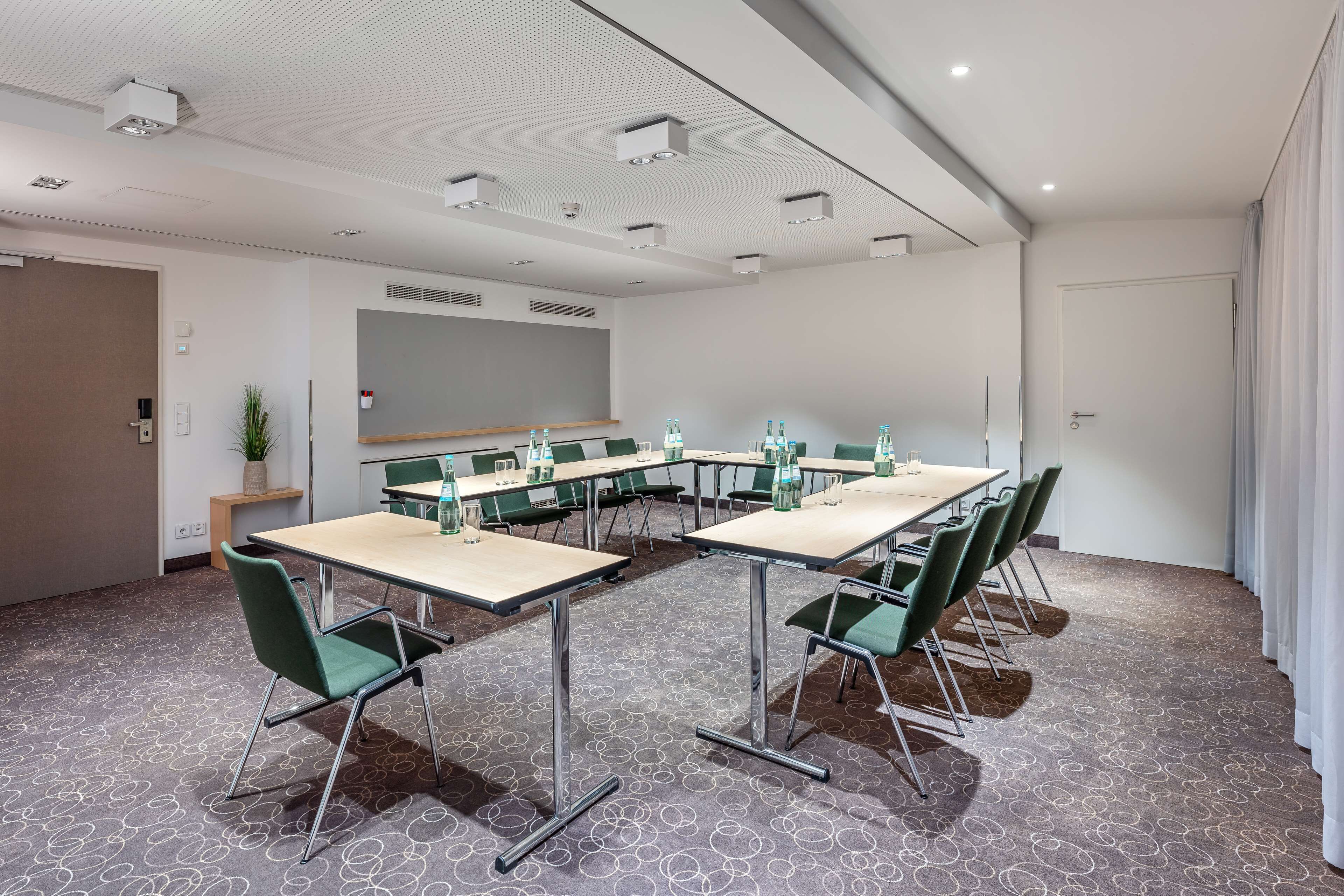 A conference room with a long table, green chairs, and a carpeted floor.