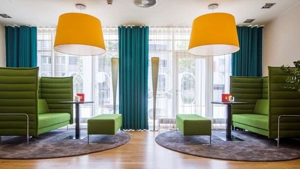 Un vestíbul modern amb sofàs verds, una taula petita i un gran finestral amb cortines color aquamarina.