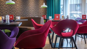 Interior modern d'un restaurant amb parets de disseny geomètric, cadires vermelles i morades, i taules amb espelmes i arxivadors vermells per als menús.