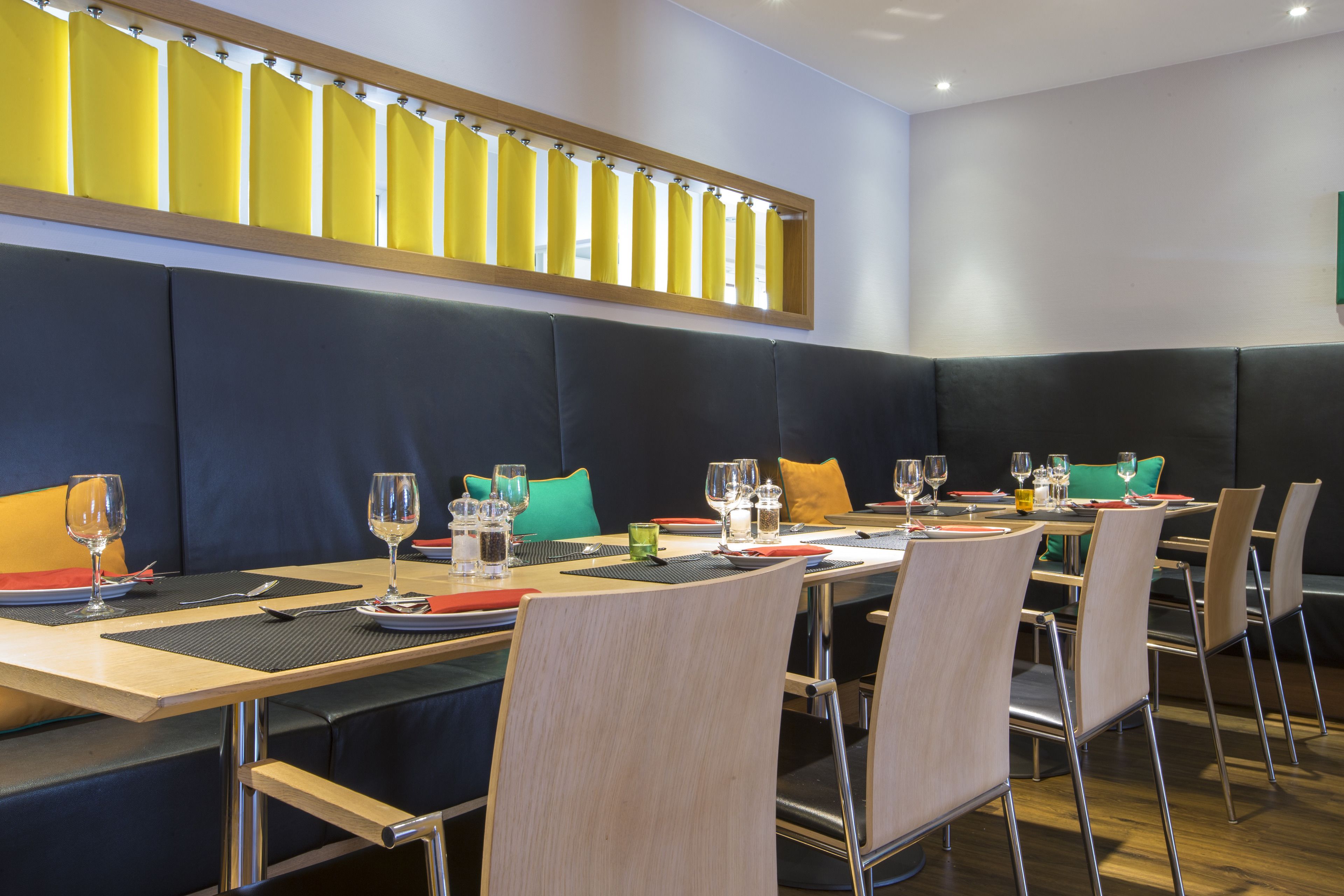 Un restaurant amb una llarga taula de menjador, molta cadira i un sostre alt amb una filera de cortines grogues.