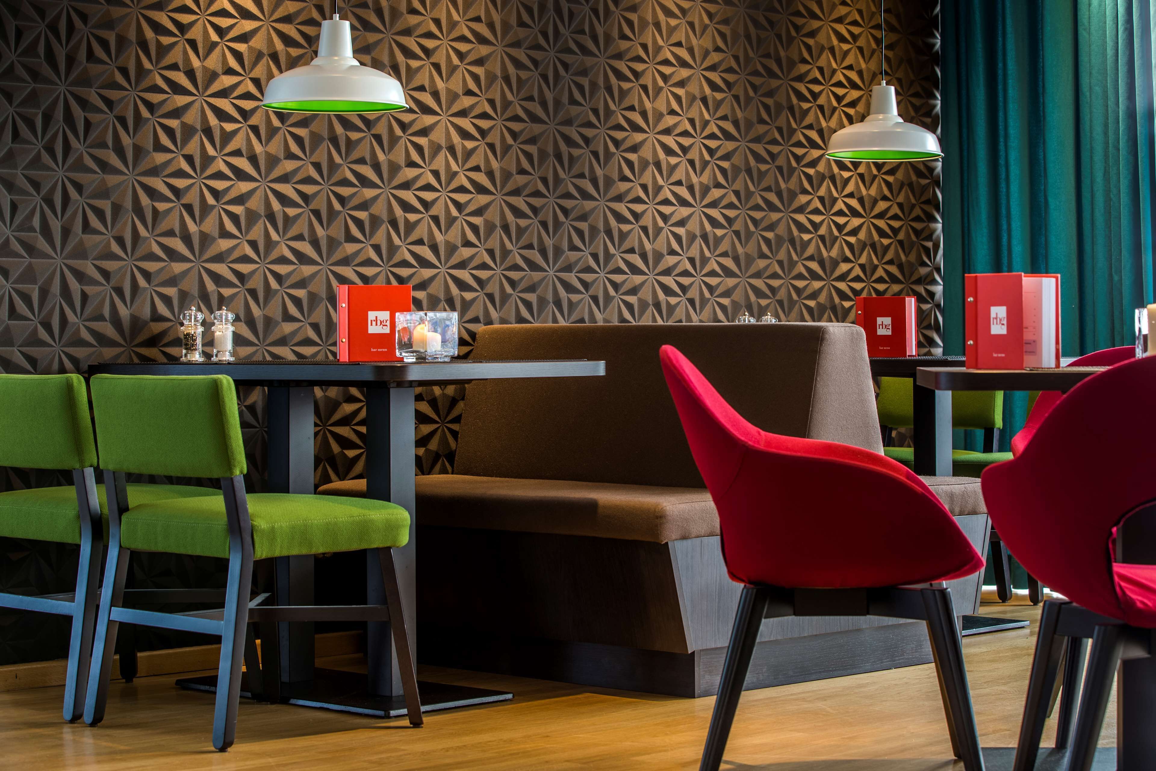 Un interior de restaurante moderno con paredes de patrón geométrico, sillas verdes y rojas, e iluminación colgante.