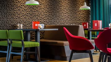 Un interior de restaurante moderno con paredes de patrón geométrico, sillas verdes y rojas, e iluminación colgante.