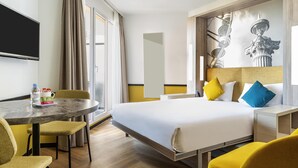 A hotel room with a bed, a desk with a chair, a television, and a large window with curtains.