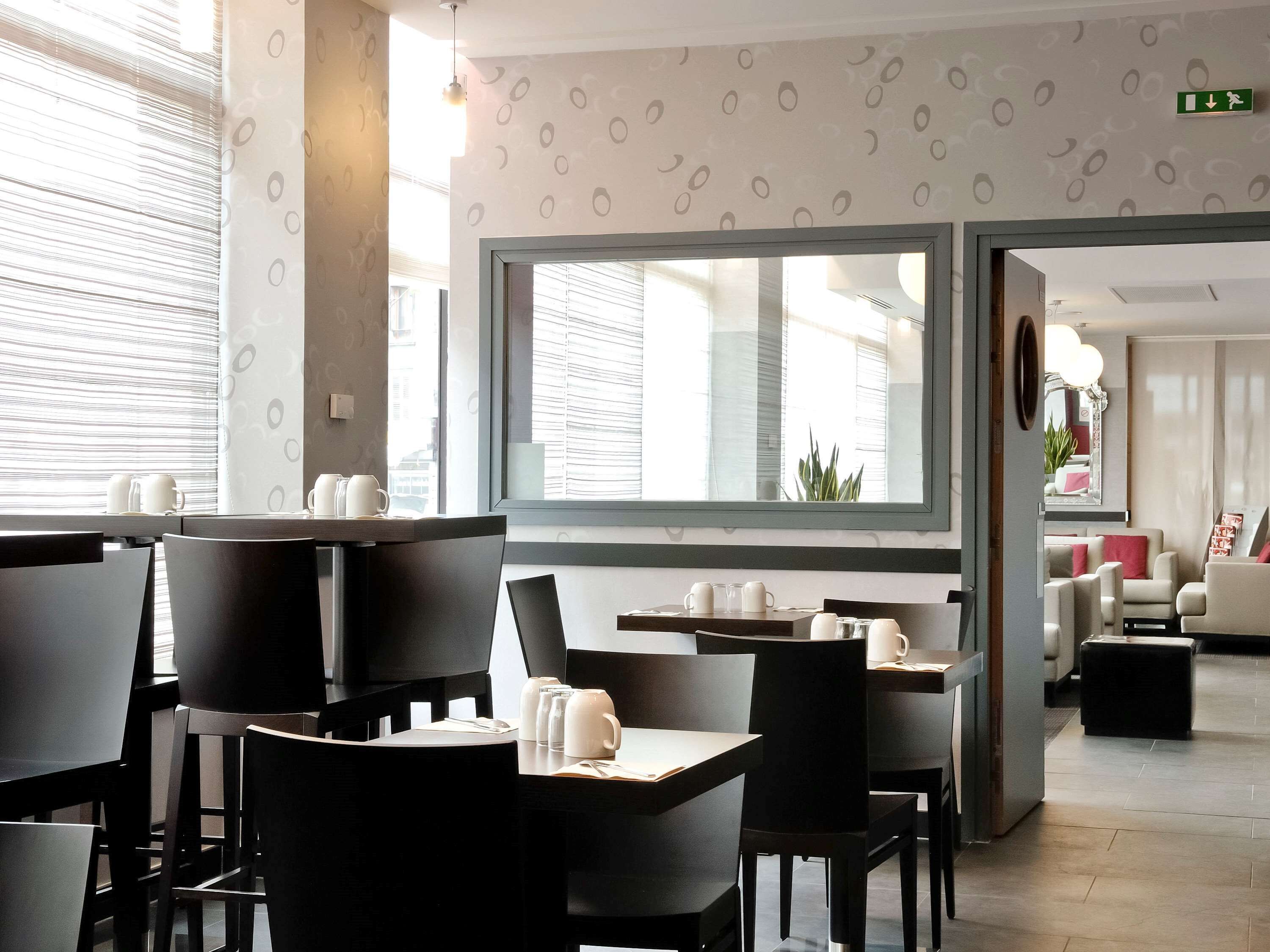 Un espace de restauration moderne, avec des tables et des chaises, une grande fenêtre équipée de stores et une vue sur la ville.