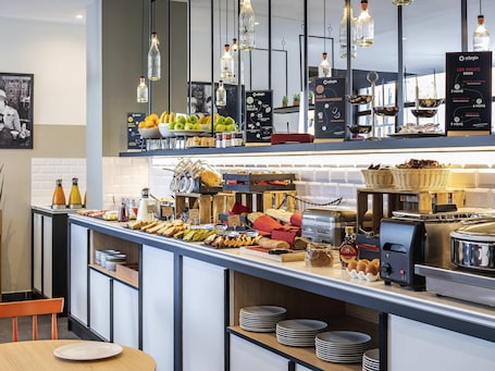 A breakfast buffet with various food items, a coffee machine, and hanging light fixtures.. Aparthotel Adagio Paris Montrouge