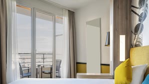 A hotel room with a large bed, a balcony with a table and chairs, and a view of the cityscape.