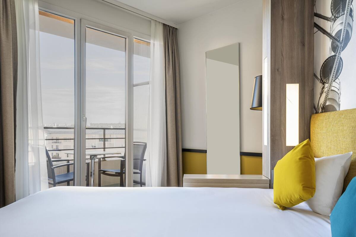 Ein Hotelzimmer mit einem großen Bett, einem Balkon mit Tisch und Stühlen und Blick auf die Stadt.